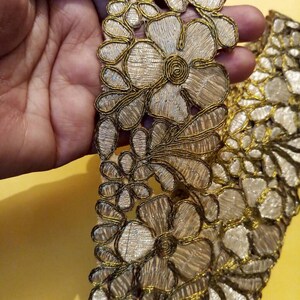 Op de afbeelding: Gouden en zilveren geborduurde bies met een bloemenmotief. De bies heeft ingewikkelde details en een delicate, vrouwelijke esthetiek.