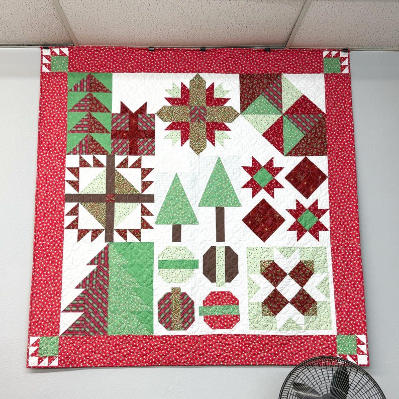 May include: A square patchwork quilt featuring a festive holiday theme with a red border. The design includes various blocks depicting Christmas trees, wrapped gifts, and geometric star patterns in shades of red, green, white, and brown.