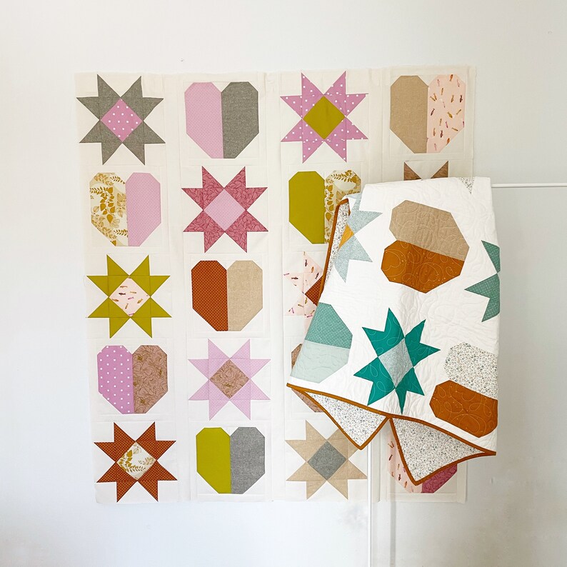 May include: A patchwork quilt with a design featuring hearts, stars, and geometric shapes in shades of pink, green, brown, and white. The quilt is made up of 16 individual squares, each with a different design. The quilt is hanging on a white wall.