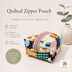 May include: A handmade, quilted zipper pouch with a patchwork design. The pouch features a pink zipper and is approximately 6" x 4" x 2". The text on the image says "Quilted Zipper Pouch" and "The perfect everyday pouch!"