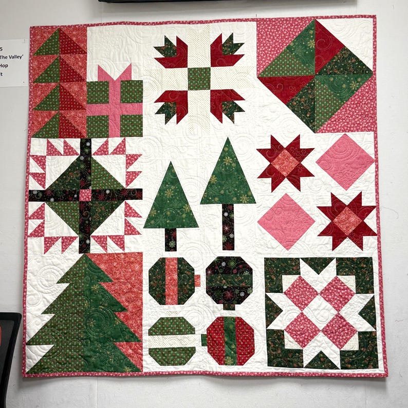May include: A square patchwork quilt featuring a white background with various holiday-themed blocks including green Christmas trees, red and green gift boxes, star patterns, and circular ornaments in shades of red, green, pink, and black fabric.