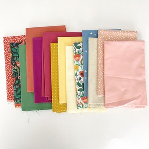 Pode incluir: Uma coleção de 14 amostras de tecido em várias cores e padrões, incluindo florais, bolinhas e cores sólidas. As amostras estão dispostas em uma fila, com as cores passando do vermelho para o amarelo para o azul.