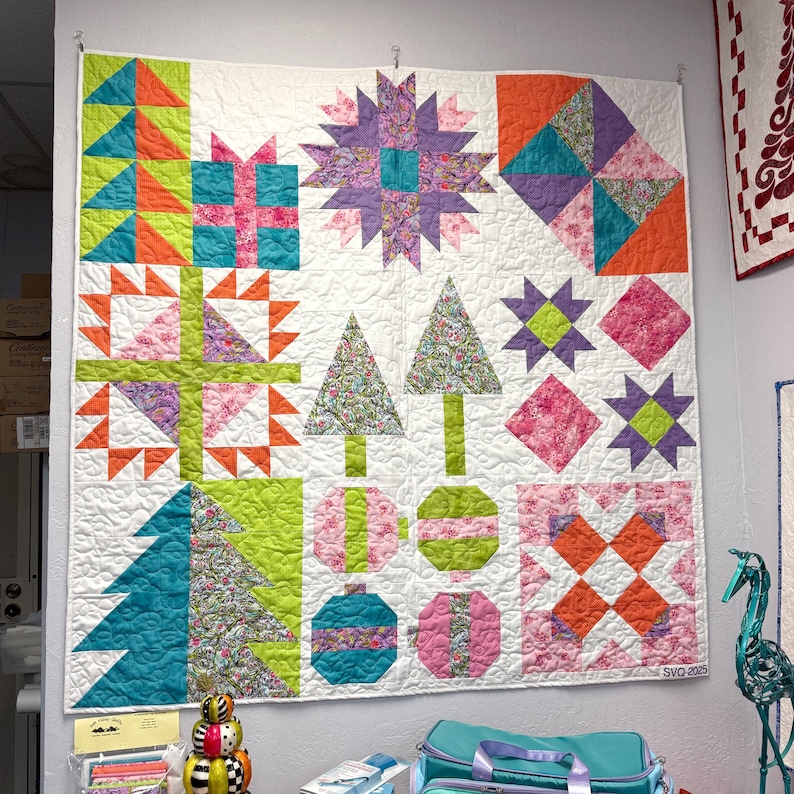 May include: A square patchwork quilt featuring a white background with various colorful blocks including geometric stars, stylized Christmas trees, gift boxes, and circular ornaments in shades of lime green, orange, purple, pink, and teal.