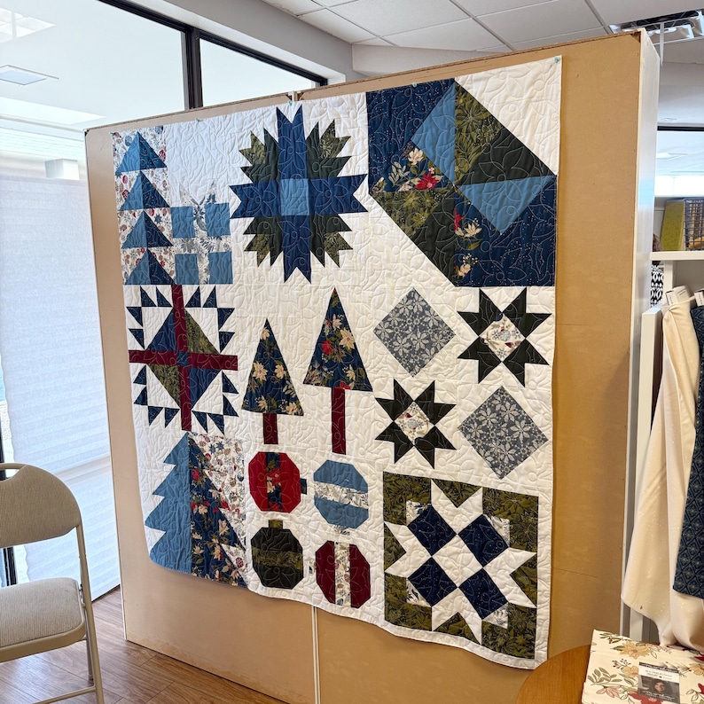 May include: A patchwork quilt featuring a white background with various block designs including blue and green stars, stylized trees, and circular ornaments. The quilt incorporates floral and geometric fabric patterns in shades of navy, forest green, red, and light blue, all stitched together with a swirling quilting pattern.