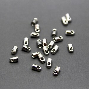 Op de afbeelding: Een groep zilveren metalen eindkappen voor koorden of het maken van sieraden. De doppen zijn klein en hebben een gat in het midden.