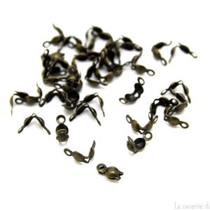 Op de afbeelding: Een stapel antieke goudkleurige metalen sluitingen voor het maken van sieraden. De sluitingen zijn gevormd als een kleine lus met een haak aan het ene uiteinde.