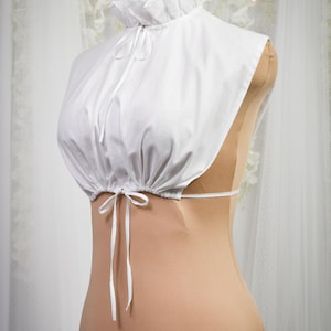 May include: White cotton lace collar with a ruffled neckline and a tie at the front. The collar is on a dress form.