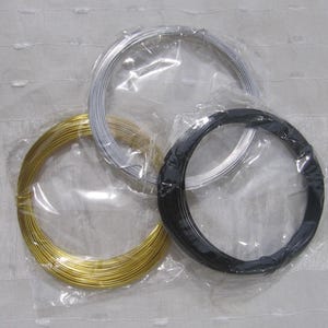 Puede incluir: Tres carretes de alambre artesanal en oro, plata y negro, cada uno enrollado y empaquetado en plástico transparente. Los alambres están bien enrollados, lo que sugiere su uso en la fabricación de joyas u otros proyectos de artesanía.