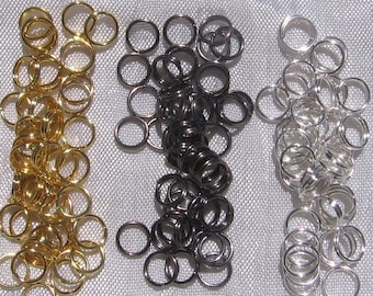 May include: Three piles of jump rings, one gold, one black, and one silver. The rings are all the same size and are arranged in a pile.