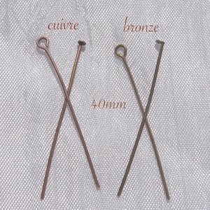 Può includere: Due spilli per la testa lunghi 40 mm, uno in rame e uno in bronzo, sono incrociati l'uno sull'altro su uno sfondo di tessuto bianco. Le parole "cuivre" e "bronze" sono scritte sopra ogni spillo.