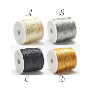 Può includere: Quattro bobine di cordoncino in diversi colori: crema, argento, nero e oro. Le bobine sono etichettate con A, B, C e D.