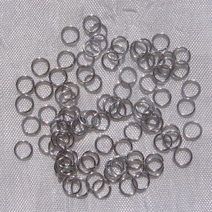 Peut inclure: Une collection de petits anneaux métalliques argentés dispersés sur une surface texturée gris clair. Les anneaux sont circulaires, d'épaisseur constante et semblent être en métal brillant. L'image est bien éclairée, soulignant l'éclat métallique des anneaux.