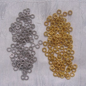 May include: Two piles of small, round metal jump rings. One pile is silver and the other is gold.