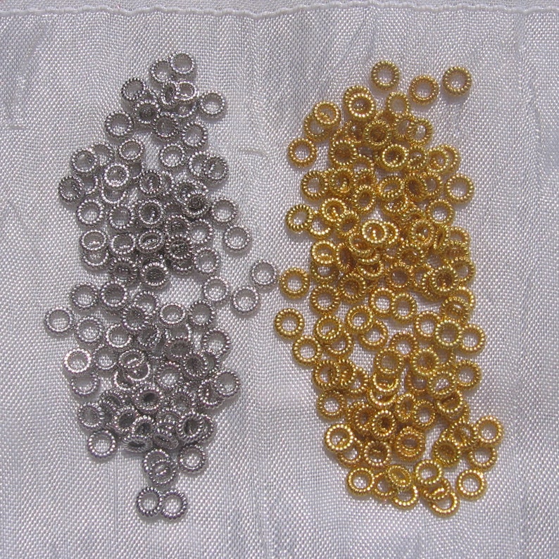 May include: Two piles of small, round metal jump rings. One pile is silver and the other is gold.