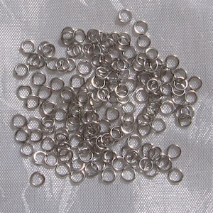 May include: A large pile of silver jump rings. The rings are small and round, and they are all linked together.