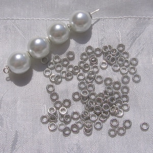 May include: A pile of silver jump rings and a strand of four white pearl beads with a silver clasp.