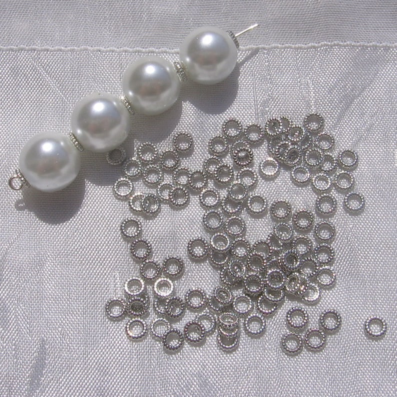 May include: A pile of silver jump rings and a strand of four white pearl beads with a silver clasp.