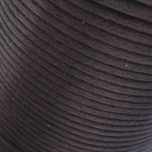 Puede incluir: Primer plano de un rollo de cuerda o cord&oacute;n marr&oacute;n oscuro, enrollado apretado. La cuerda tiene una superficie lisa y ligeramente texturizada.