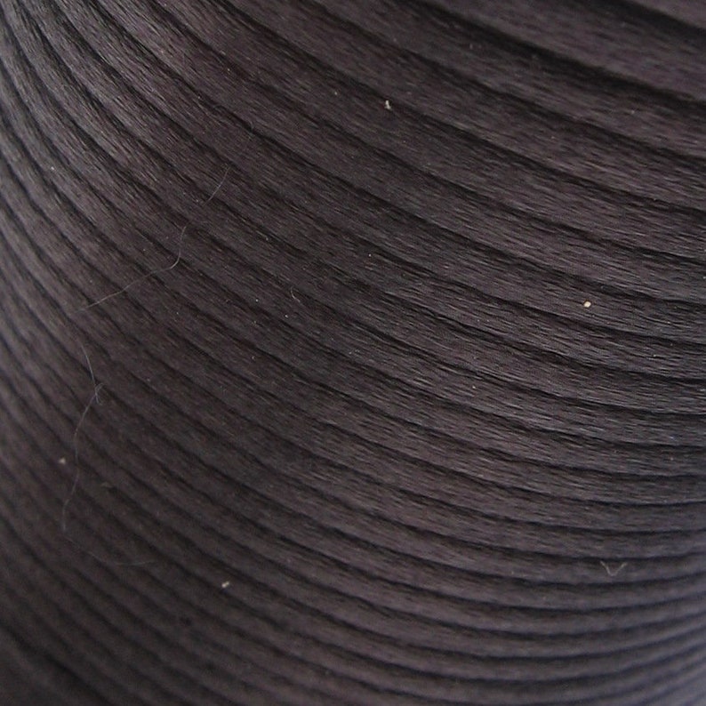 Puede incluir: Primer plano de un rollo de cuerda o cord&oacute;n marr&oacute;n oscuro, enrollado apretado. La cuerda tiene una superficie lisa y ligeramente texturizada.