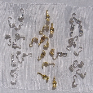 Peut inclure: Un assortiment de fermoirs en métal argenté et doré pour la fabrication de bijoux. Les fermoirs sont disposés sur un fond en tissu blanc.
