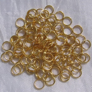 May include: A large pile of gold jump rings. The rings are all the same size and are arranged in a random pattern.