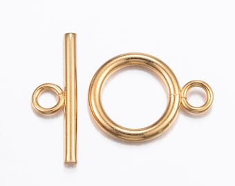 May include: A gold-colored toggle clasp, featuring a circular ring with a small loop and a straight bar with a loop. The clasp is designed for jewelry making and is shown against a white background.