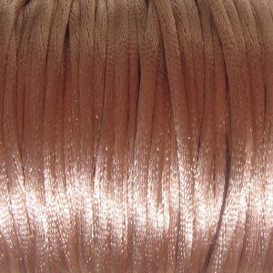 Puede incluir: Primer plano de un carrete de cord&oacute;n de sat&eacute;n marr&oacute;n claro. El cord&oacute;n es liso y brillante, y est&aacute; enrollado firmemente alrededor del carrete.