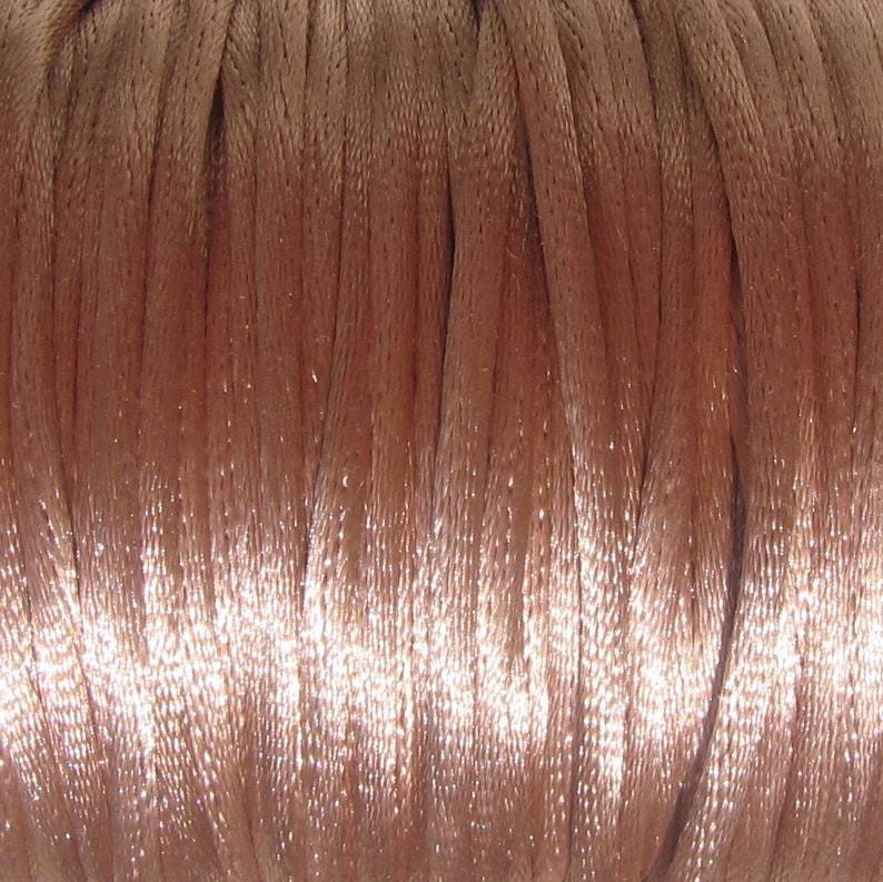 Puede incluir: Primer plano de un carrete de cord&oacute;n de sat&eacute;n marr&oacute;n claro. El cord&oacute;n es liso y brillante, y est&aacute; enrollado firmemente alrededor del carrete.