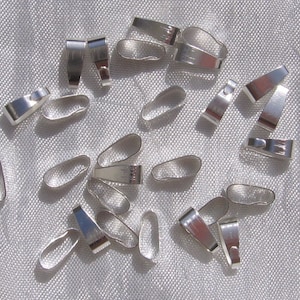 Peut inclure: Une collection de petits apprêts de bijoux argentés et brillants, comprenant des connecteurs de bélière et des boucles ovales. Les apprêts sont dispersés sur une surface texturée et claire, de formes et de tailles variées.