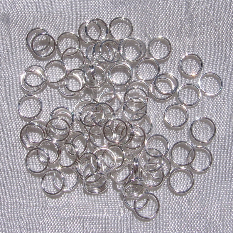 May include: A large pile of silver jump rings. The rings are all the same size and are arranged in a random pattern.