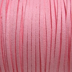 May include: Close-up of a spool of pink leather cord. The cord is made of thin, flat strips of leather that are woven together.