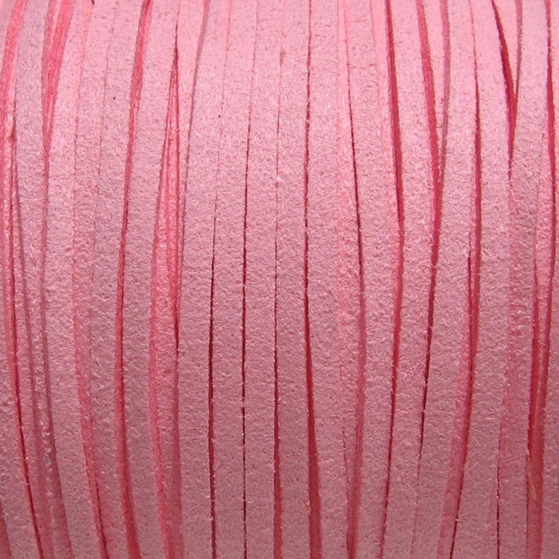 May include: Close-up of a spool of pink leather cord. The cord is made of thin, flat strips of leather that are woven together.