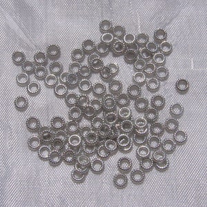 May include: A large pile of silver jump rings, a type of jewelry finding, on a white fabric background.