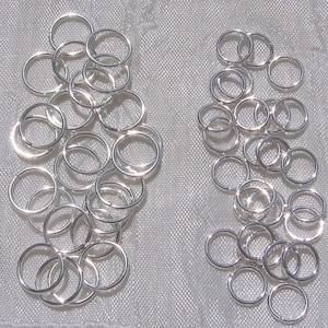 Peut inclure: Un grand tas d'anneaux de saut argentés, un matériau de fabrication de bijoux populaire, sur un fond de tissu blanc.