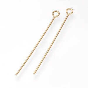 May include: Two gold-coloured eye pins, each with a looped top and a straight, slender body. The pins are angled slightly, resting against a white background. These jewellery-making components are ideal for crafting earrings, pendants, and other accessories.
