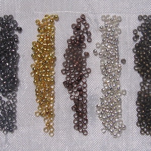 May include: Five rows of small, round beads in different colors. The beads are arranged in rows, with each row containing a different color. The colors are black, gold, brown, silver, and bronze.