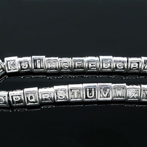 May include: A silver alphabet bead bracelet with the letters A through Z. The beads are in a square shape and are strung on a silver chain.
