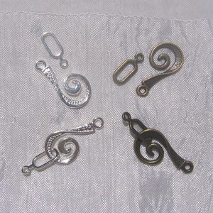 Op de afbeelding: Vier metalen sluitingen met een swirl-ontwerp. Twee zijn zilver en twee zijn brons.
