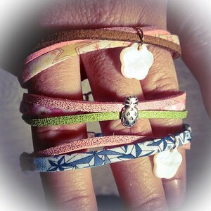 May include: Four layered bracelets with different patterns and colors. The bracelets feature a pineapple charm and a white flower charm.