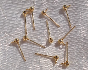 May include: A collection of gold-toned metal earring posts, each featuring a small spherical ball at the top and a tiny loop at the base for attaching charms or dangles. These jewelry components are arranged in a scattered pattern.
