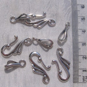 Puede incluir: Seis cierres de metal plateados con dise&ntilde;os intrincados. Los cierres tienen forma de gancho con un ala decorativa a cada lado. Los cierres miden aproximadamente 2,5 cm de largo.