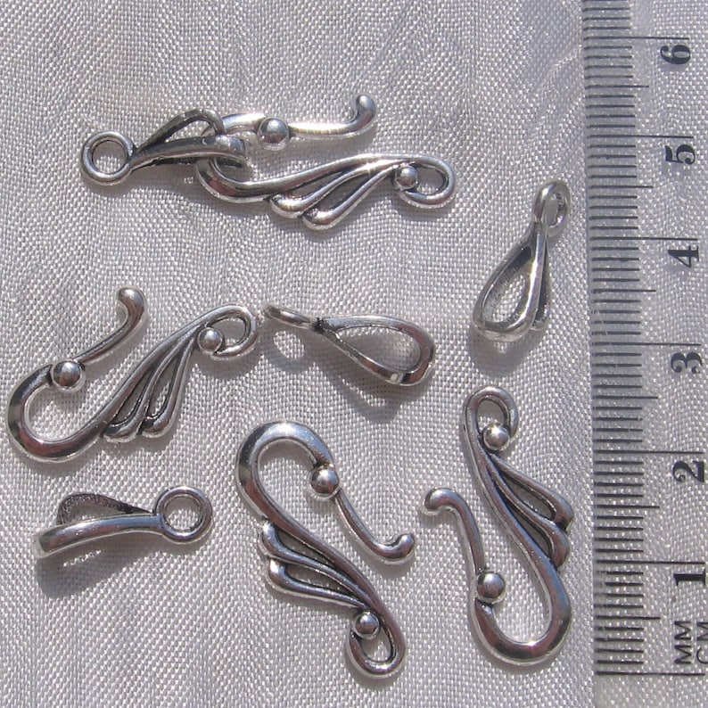 Puede incluir: Seis cierres de metal plateados con dise&ntilde;os intrincados. Los cierres tienen forma de gancho con un ala decorativa a cada lado. Los cierres miden aproximadamente 2,5 cm de largo.