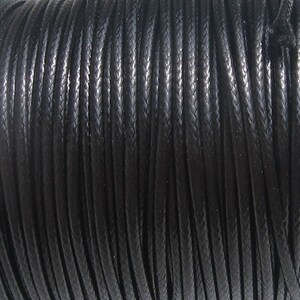 May include: A continuous length of black cord featuring a tightly woven, braided texture. The cord is arranged in parallel, vertical strands, showcasing a consistent, smooth, and uniform surface finish throughout the entire length of the material.