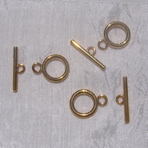 Op de afbeelding: Vijf goudkleurige metalen toggle-sluitingen voor het maken van sieraden. Elke sluiting heeft een ronde ring en een rechte staaf.