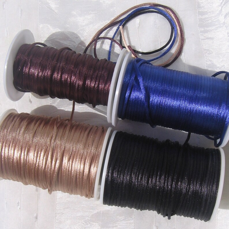 Puede incluir: Cuatro carretes de cord&oacute;n de sat&eacute;n en marr&oacute;n, azul, beige y negro. Los cordones est&aacute;n enrollados alrededor de carretes de pl&aacute;stico blanco.