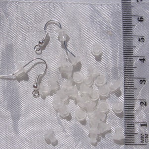 Puede incluir: Un juego de respaldos de pendientes de plástico transparente y dos ganchos de pendientes de plata. Los respaldos de los pendientes son pequeños y redondos, y los ganchos son simples y elegantes.