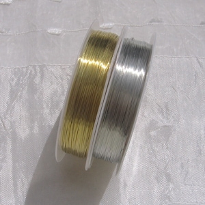 Puede incluir: Dos carretes de alambre, uno dorado y otro plateado, están enrollados alrededor de carretes de plástico transparente. Los carretes están apilados uno encima del otro.