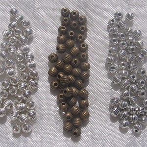 May include: Three piles of metal beads. The beads are silver, bronze, and antique gold. The beads are round and have a ribbed texture.