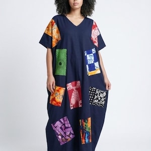 Puede incluir: Un vestido azul marino de manga corta con cuello en V. El vestido presenta parches estampados de colores en varias formas y tamaños. Los parches incluyen diseños en naranja, verde, rojo y morado. El vestido es holgado y fluido.