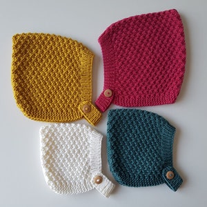 Op de afbeelding: Vier gebreide baby mutsjes in verschillende kleuren: geel, rood, wit en groen. Elk mutsje heeft een houten knoop.